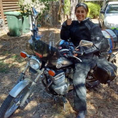 Ulrike at the end of the trip sitting on the motorcycle looking happy, dusty, and thumbs up in Australia.