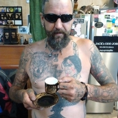 Brett the hero with no shirt, lots of tattoos, drinking coffee from a vintage cup and saucer.